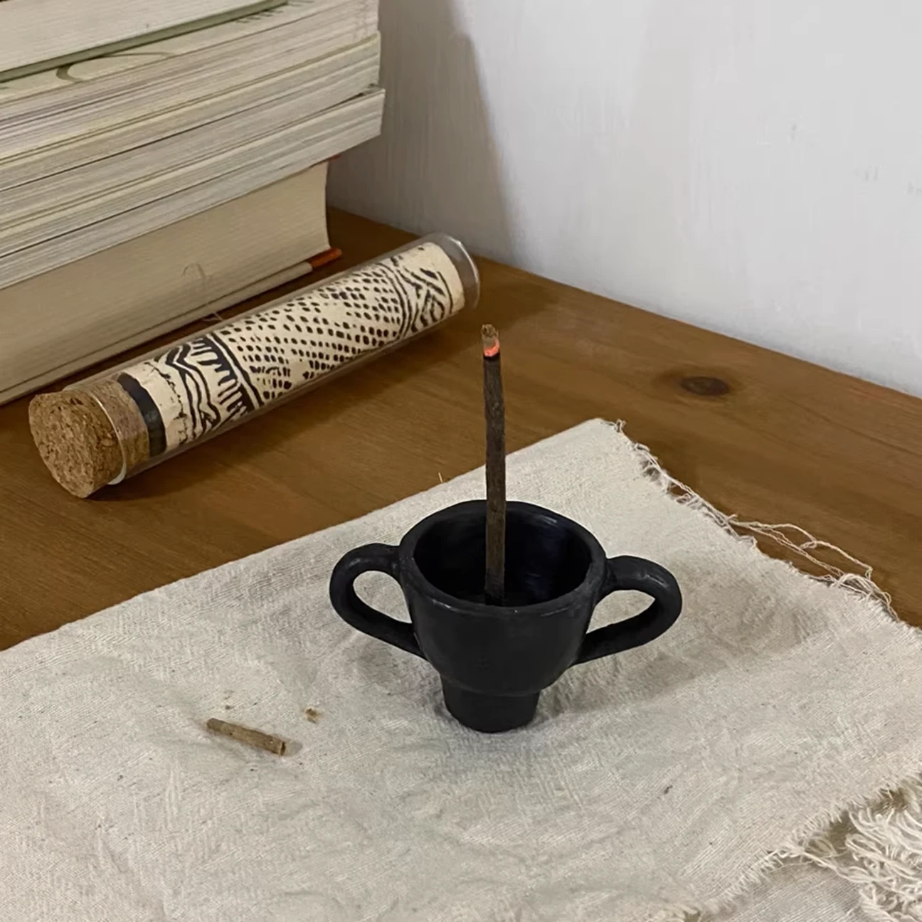 Functional scene of a hand-pinched black pottery incense holder with rising incense smoke.