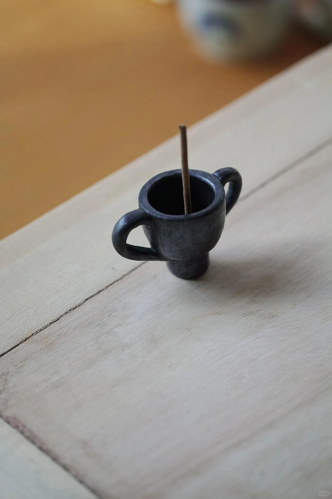 Tibetan black pottery incense holder in use on a rustic wooden desk.