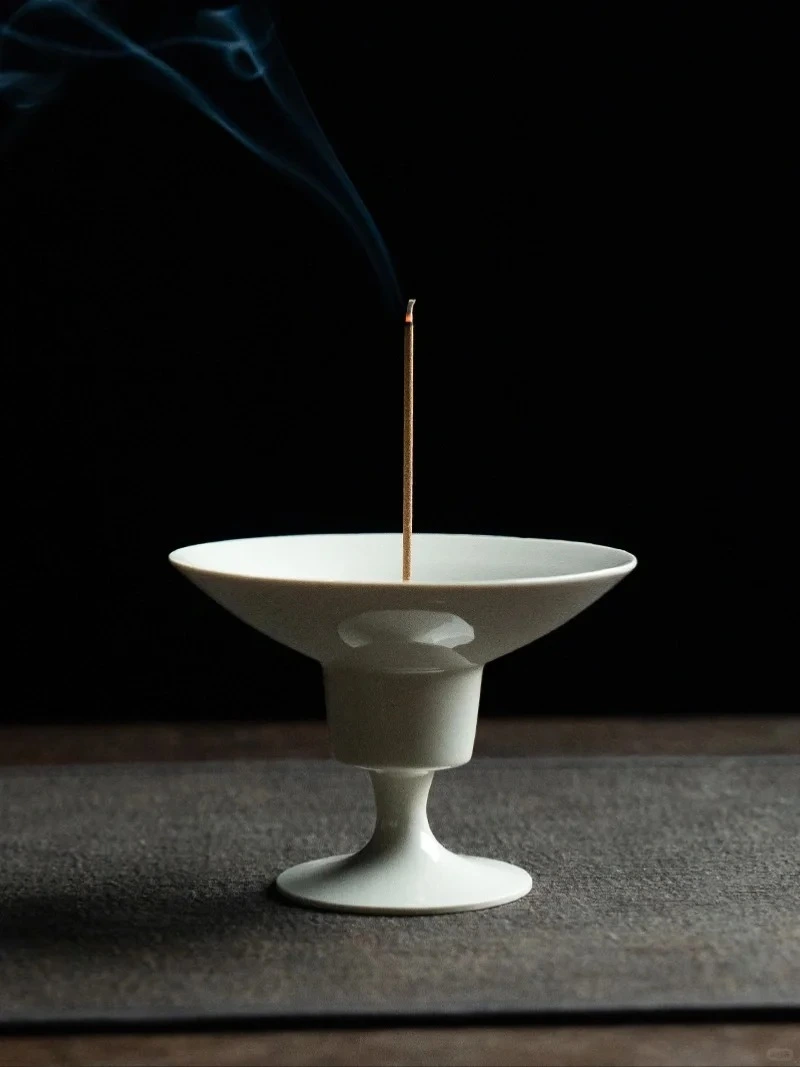 A minimalist Dehua Blanc de Chine high-foot incense holder for meditation, featuring a single stick incense burning with a wisp of smoke, set against a dark, serene background. This Song Dynasty-inspired ceramic burner is designed for Zen practice.